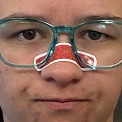 A picture of Captain Atlas. Close up, wearing blue glasses and with a somewhat annoyed expression, a red bandage across his nose.